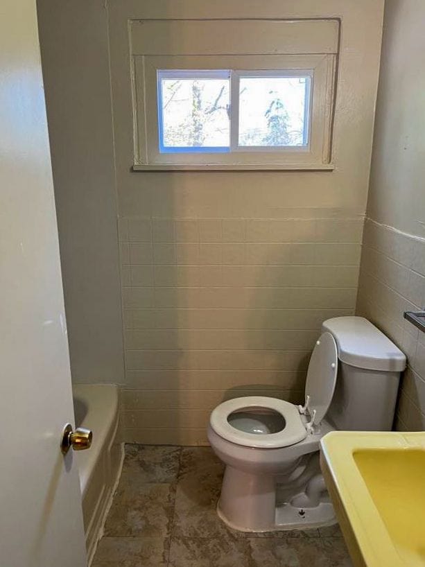 bathroom with a bathing tub, a wealth of natural light, tile walls, and toilet