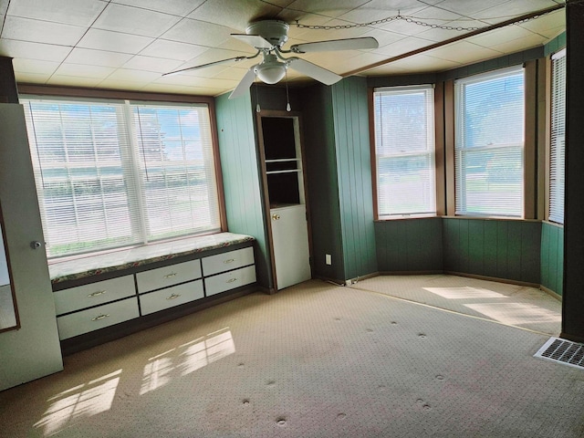 unfurnished bedroom featuring light colored carpet, ceiling fan, and wood walls