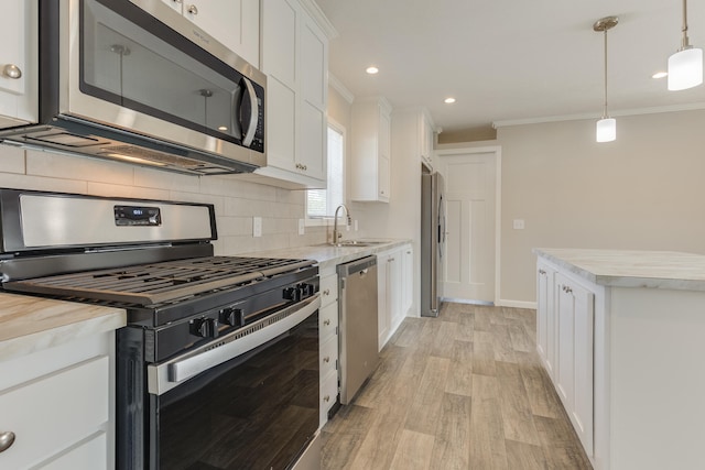 kitchen with stainless steel appliances, crown molding, sink, decorative light fixtures, and white cabinetry