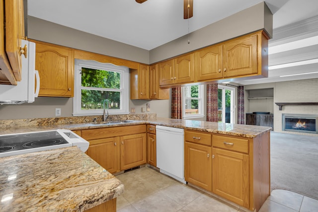 kitchen with dishwasher, light carpet, a fireplace, light stone counters, and kitchen peninsula