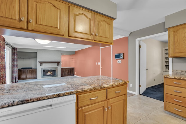 kitchen with dishwasher, light stone counters, light tile patterned floors, and a brick fireplace