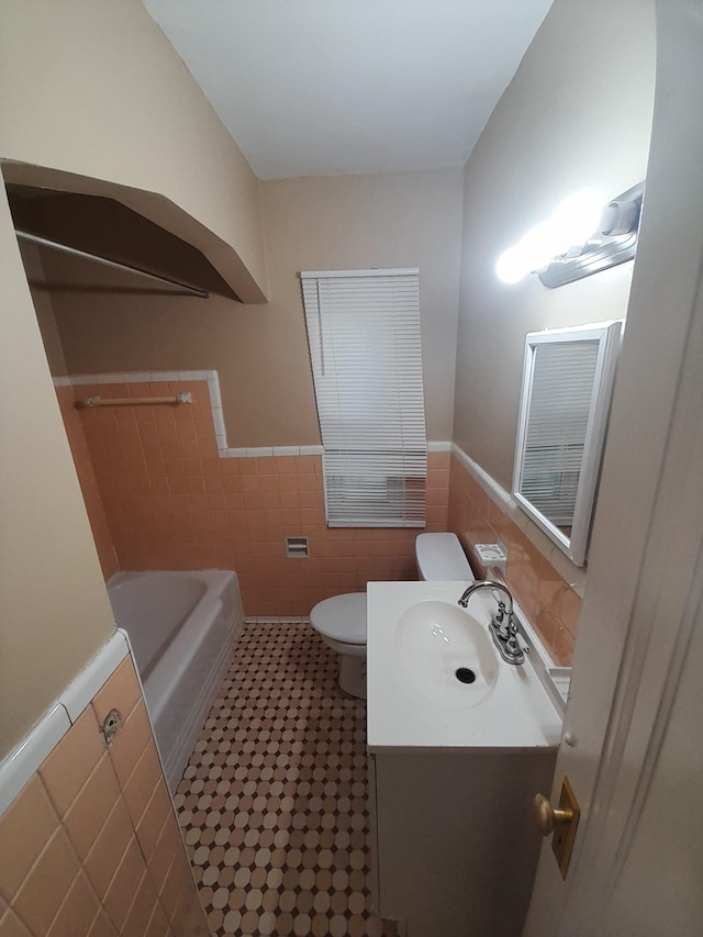 bathroom with vanity, a bathtub, toilet, and tile walls