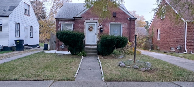 bungalow with a shingled roof, a front yard, and brick siding