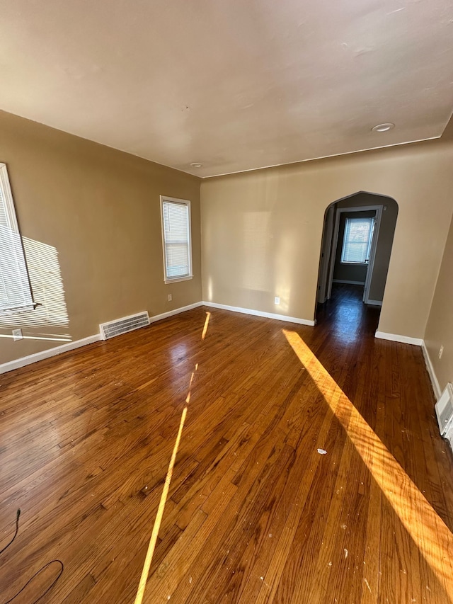 unfurnished living room with hardwood / wood-style flooring, baseboards, visible vents, and arched walkways