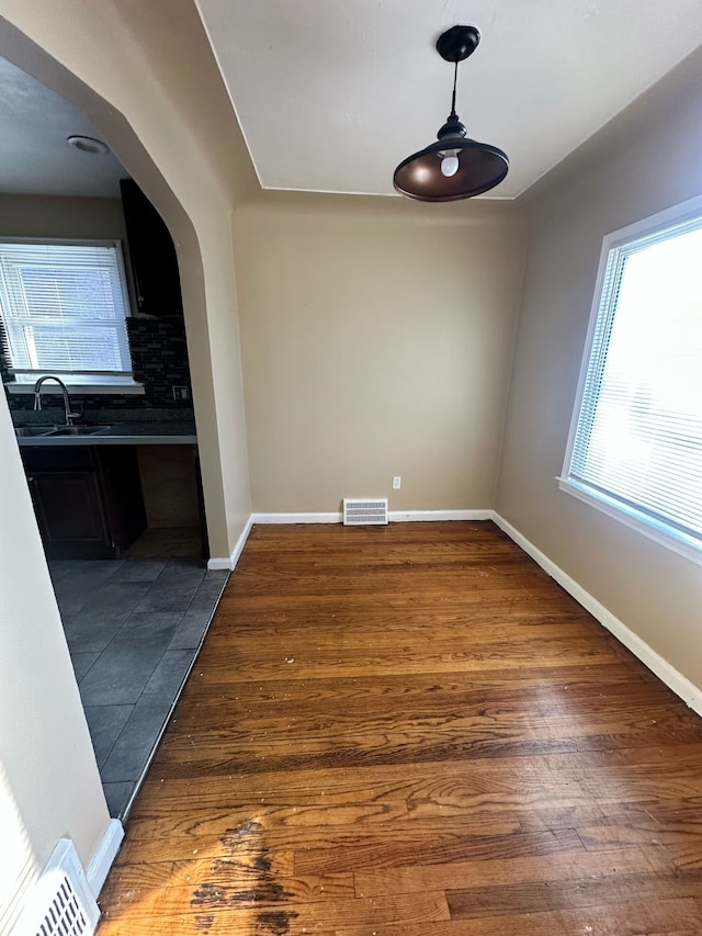 unfurnished dining area featuring visible vents, arched walkways, a sink, and wood finished floors