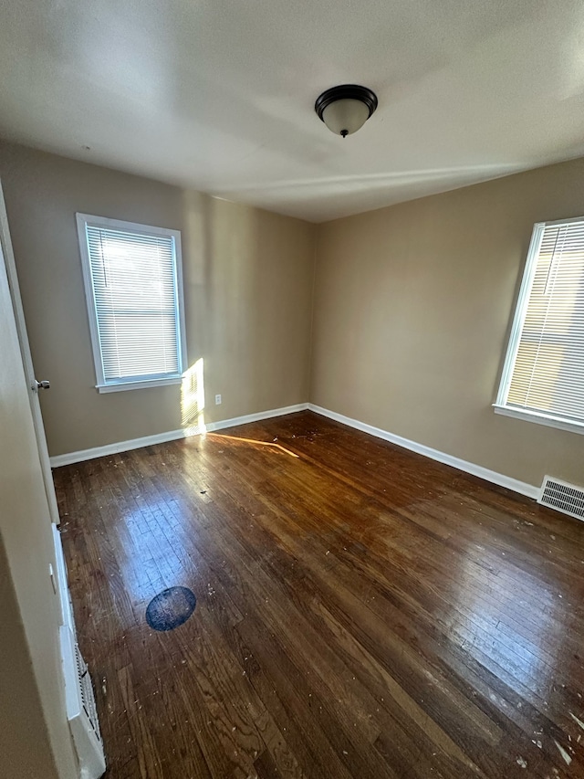 empty room featuring a wealth of natural light, wood-type flooring, visible vents, and baseboards