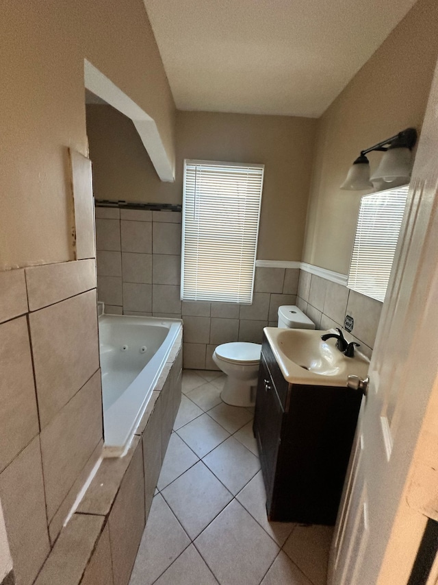 bathroom featuring toilet, a tub with jets, tile patterned floors, vanity, and tile walls