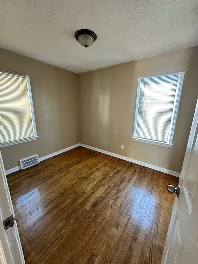 unfurnished room with visible vents, a textured ceiling, baseboards, and hardwood / wood-style flooring