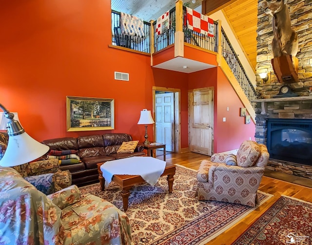 living room featuring hardwood / wood-style floors, beam ceiling, a stone fireplace, and high vaulted ceiling