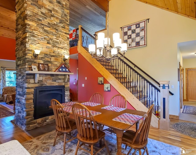 dining room with a stone fireplace, high vaulted ceiling, a notable chandelier, wood-type flooring, and wood ceiling