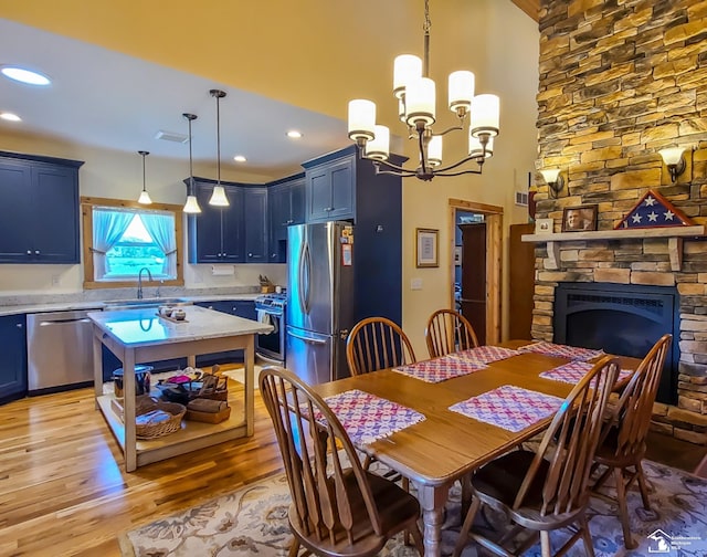 dining space featuring a stone fireplace, sink, an inviting chandelier, and light wood-type flooring