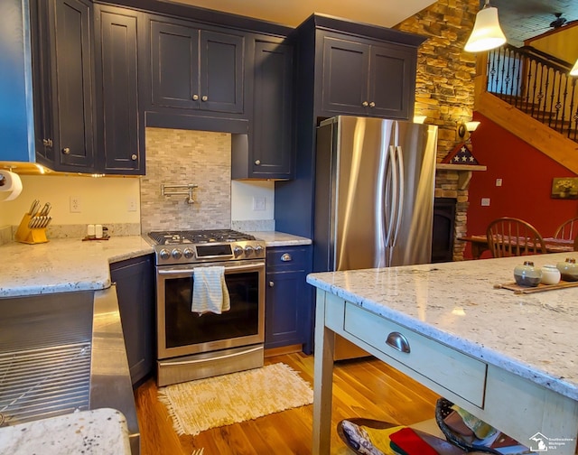 kitchen with a stone fireplace, hanging light fixtures, light stone countertops, light wood-type flooring, and appliances with stainless steel finishes