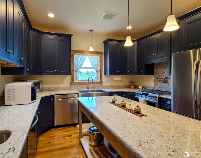 kitchen with sink, hanging light fixtures, light stone counters, appliances with stainless steel finishes, and light wood-type flooring