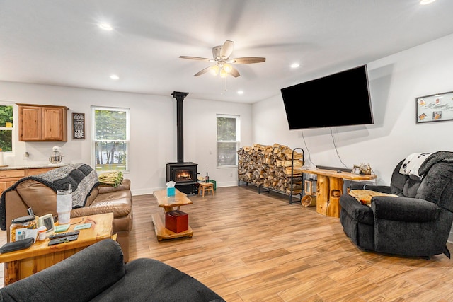 living room with a wood stove, ceiling fan, and light hardwood / wood-style floors