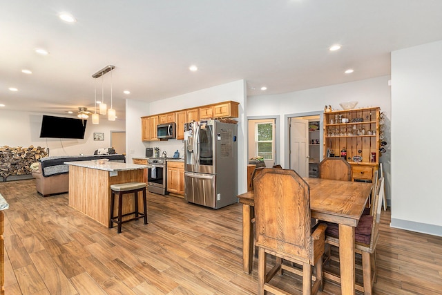 kitchen with appliances with stainless steel finishes, decorative light fixtures, light stone counters, and light hardwood / wood-style floors