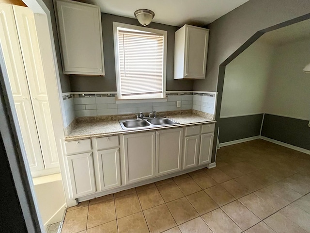 kitchen featuring decorative backsplash, white cabinetry, sink, and light tile patterned floors