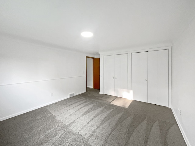 unfurnished bedroom with dark colored carpet and multiple closets