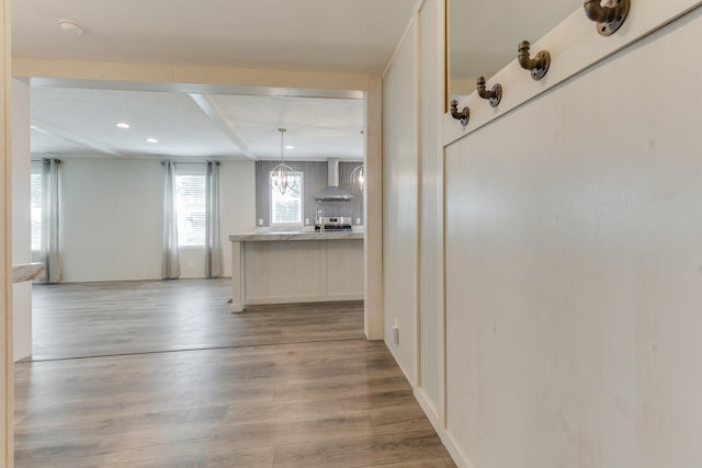 kitchen featuring light wood-type flooring, backsplash, wall chimney range hood, beam ceiling, and hanging light fixtures