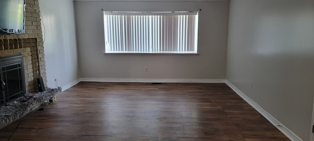 unfurnished living room featuring a healthy amount of sunlight, dark hardwood / wood-style flooring, and a brick fireplace