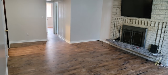 unfurnished living room featuring dark wood-type flooring and a brick fireplace