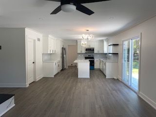 kitchen featuring dark hardwood / wood-style flooring, ceiling fan with notable chandelier, stainless steel appliances, a kitchen island, and white cabinetry