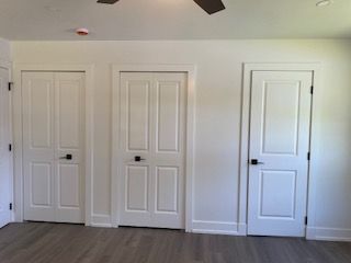 unfurnished bedroom with ceiling fan, dark wood-type flooring, and multiple closets