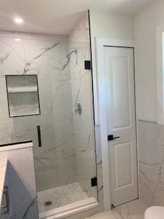 bathroom featuring vanity, toilet, a shower with door, and tile walls