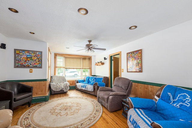 living room with a textured ceiling, wood-type flooring, a baseboard heating unit, wooden walls, and ceiling fan