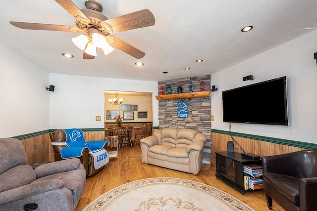 living room with a textured ceiling, wood-type flooring, ceiling fan with notable chandelier, and wood walls