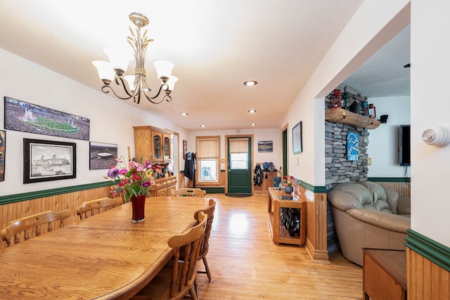 dining area with a notable chandelier, wooden walls, and light hardwood / wood-style flooring