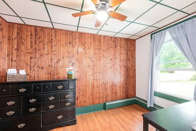 unfurnished bedroom with wood walls, ceiling fan, wood-type flooring, and a drop ceiling