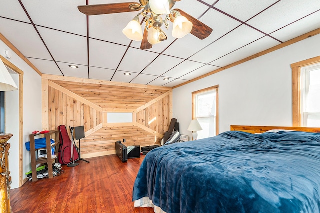 bedroom with ceiling fan, dark hardwood / wood-style floors, crown molding, and wooden walls