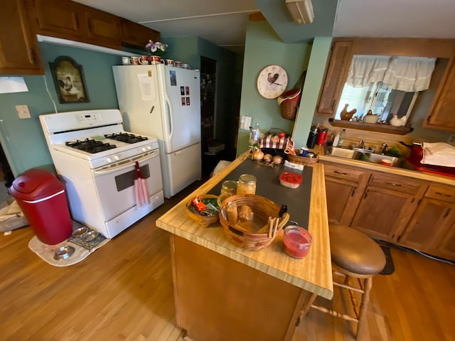 kitchen with a breakfast bar, sink, white appliances, and light wood-type flooring