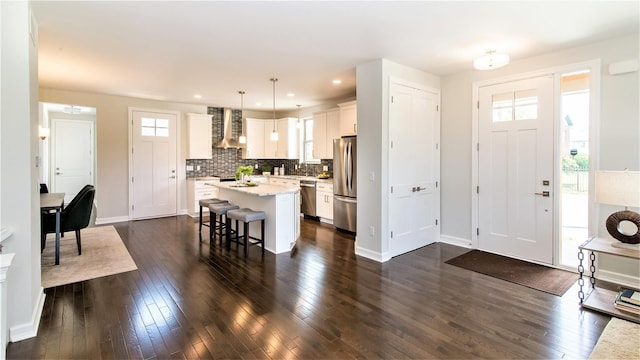 kitchen with wall chimney exhaust hood, stainless steel appliances, pendant lighting, white cabinets, and a center island