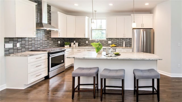 kitchen featuring a kitchen island, decorative light fixtures, wall chimney range hood, and appliances with stainless steel finishes