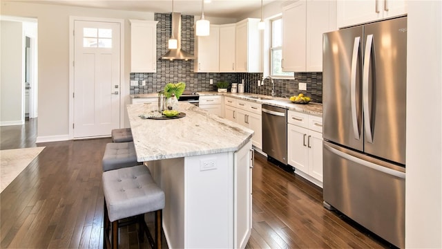 kitchen featuring a center island, stainless steel appliances, white cabinetry, and wall chimney range hood