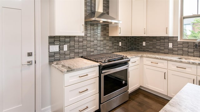 kitchen with stainless steel gas range oven, sink, white cabinets, and wall chimney range hood