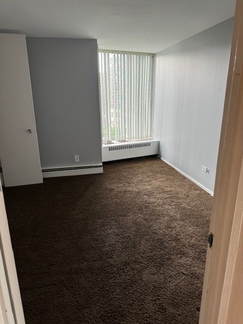 unfurnished room with dark carpet, radiator heating unit, and baseboard heating