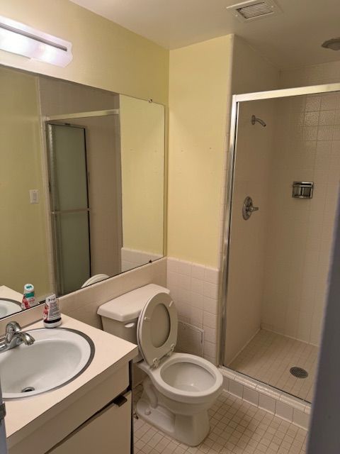 bathroom with tile patterned floors, a shower with door, vanity, and toilet