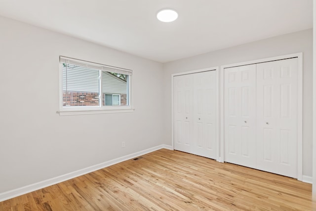 unfurnished bedroom with light hardwood / wood-style floors and two closets