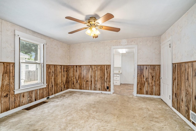 spare room with wooden walls, ceiling fan, and light colored carpet