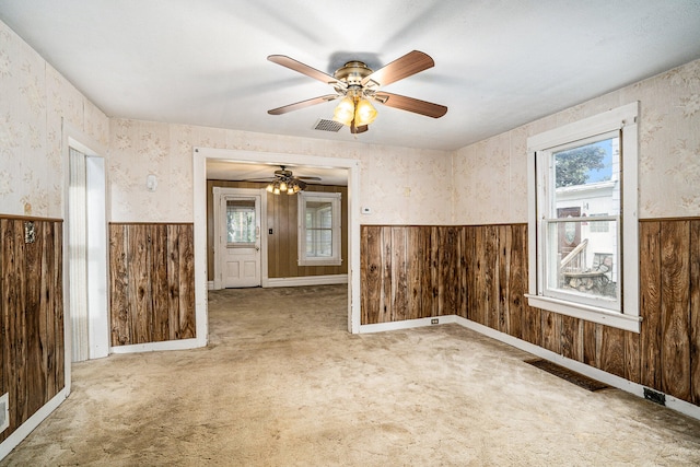 unfurnished room with wooden walls, ceiling fan, and light colored carpet