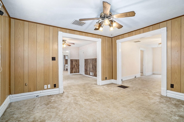 empty room featuring light carpet, ceiling fan, and wood walls