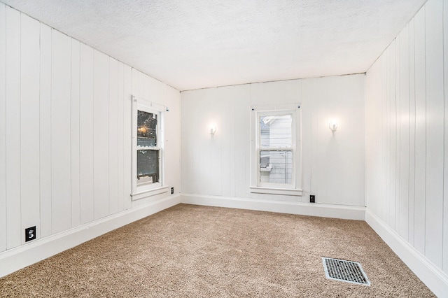 empty room with carpet, a textured ceiling, and wooden walls