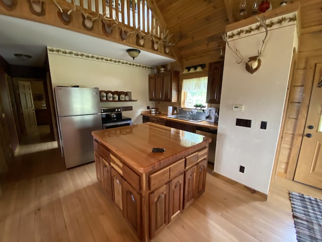 kitchen with light wood-type flooring, stainless steel appliances, a kitchen island, and vaulted ceiling