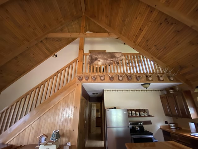 kitchen with beam ceiling, stainless steel appliances, high vaulted ceiling, and wooden walls