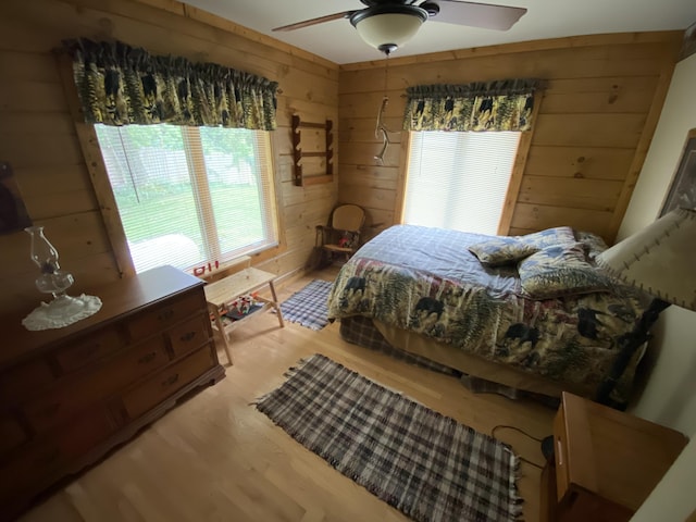 bedroom with hardwood / wood-style floors, ceiling fan, and wooden walls