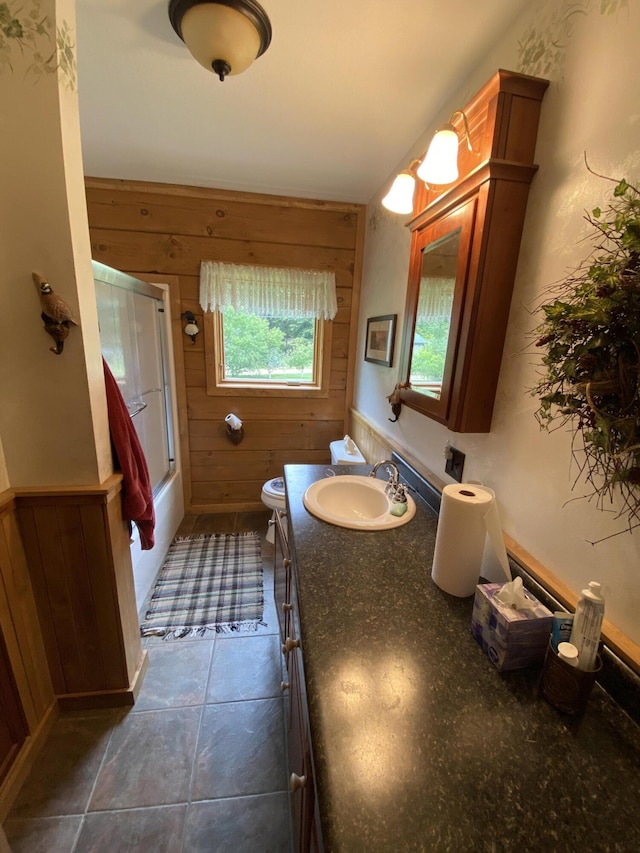 full bathroom featuring vanity, shower / bath combination with glass door, tile patterned flooring, toilet, and wood walls