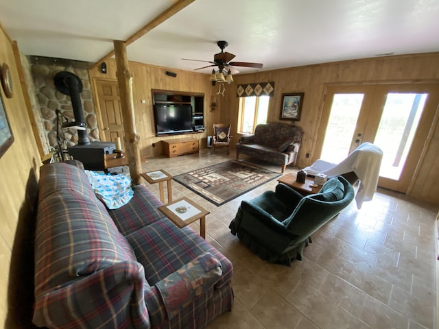 living room featuring a wood stove, french doors, wooden walls, ceiling fan, and beamed ceiling