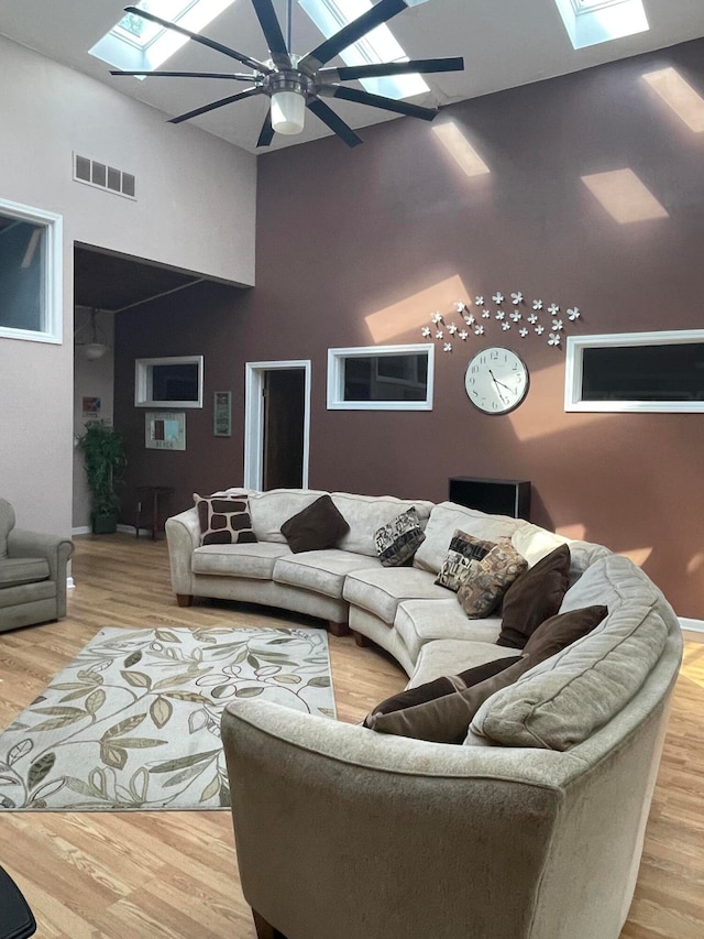 living room featuring ceiling fan, light hardwood / wood-style floors, high vaulted ceiling, and a skylight